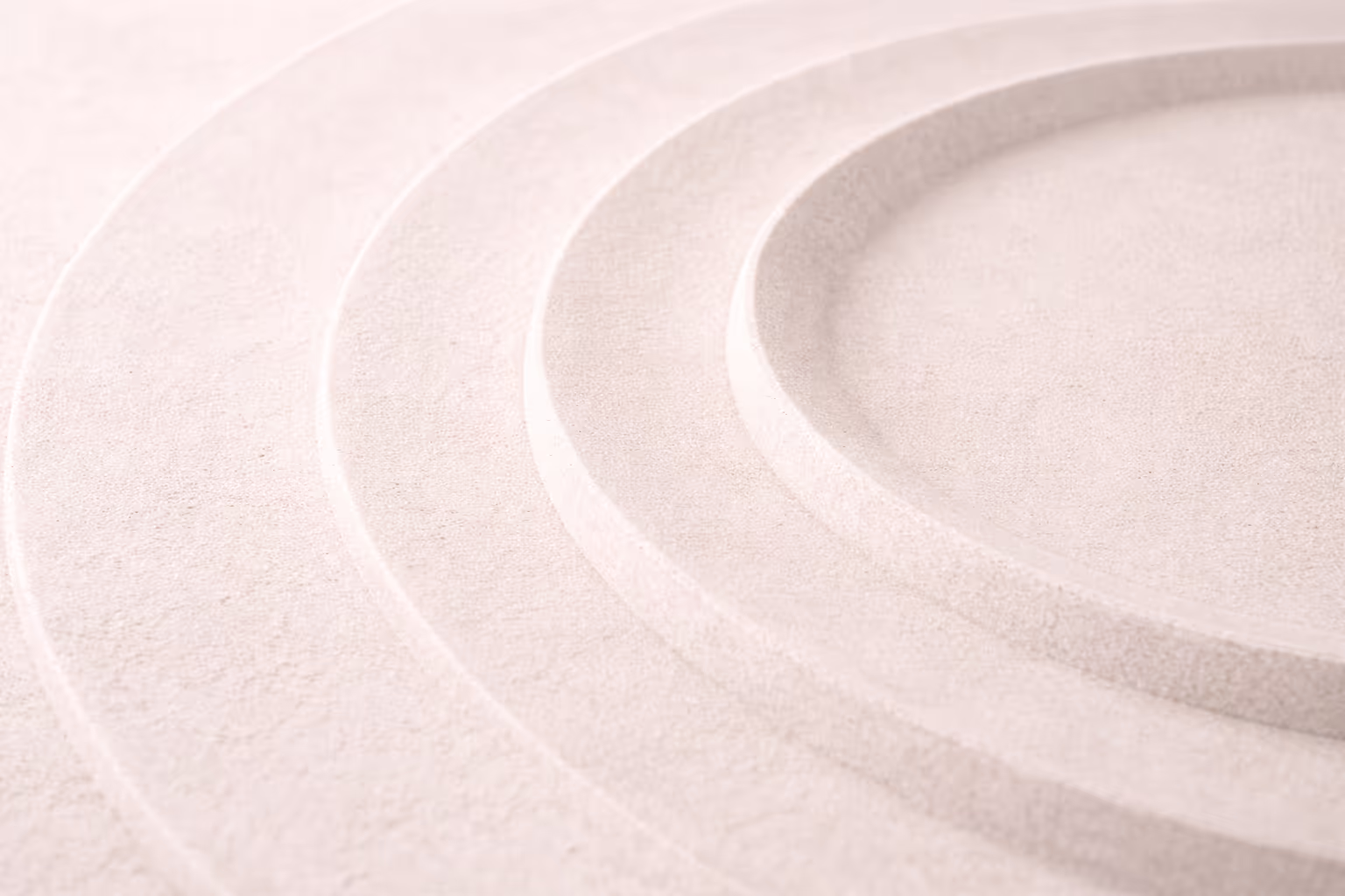 A close-up of concentric rings in light stone or sand, shot in soft diffuse light, with clean negative space on one side.
