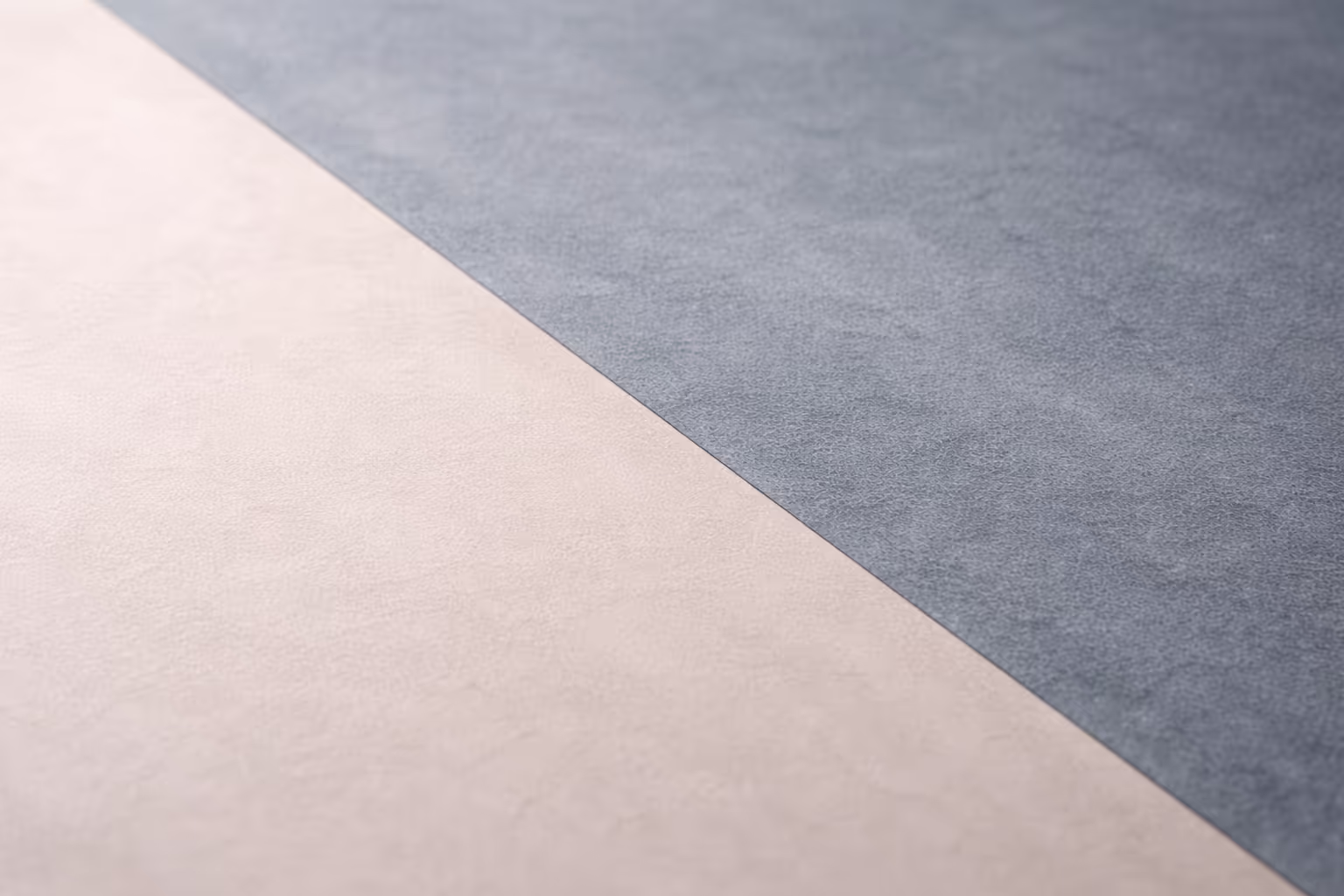 Two contrasting matte textures meeting along a soft diagonal line, one warm grey and one cool slate, on a neutral background with ample negative space.