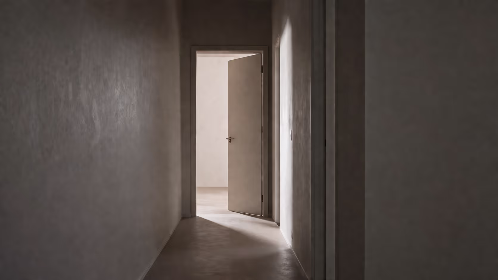  A dimly lit empty corridor with a single door left slightly ajar at the far end, muted grey and warm tones, soft diffused light.
