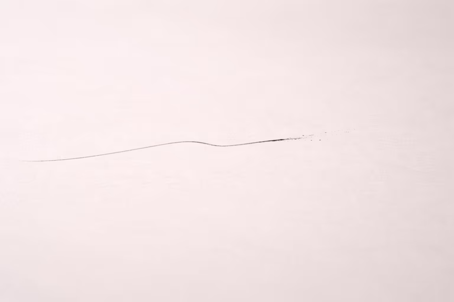 a single thin graphite mark crossing a pale, slightly textured surface, leaving a faint trace at the point of interruption