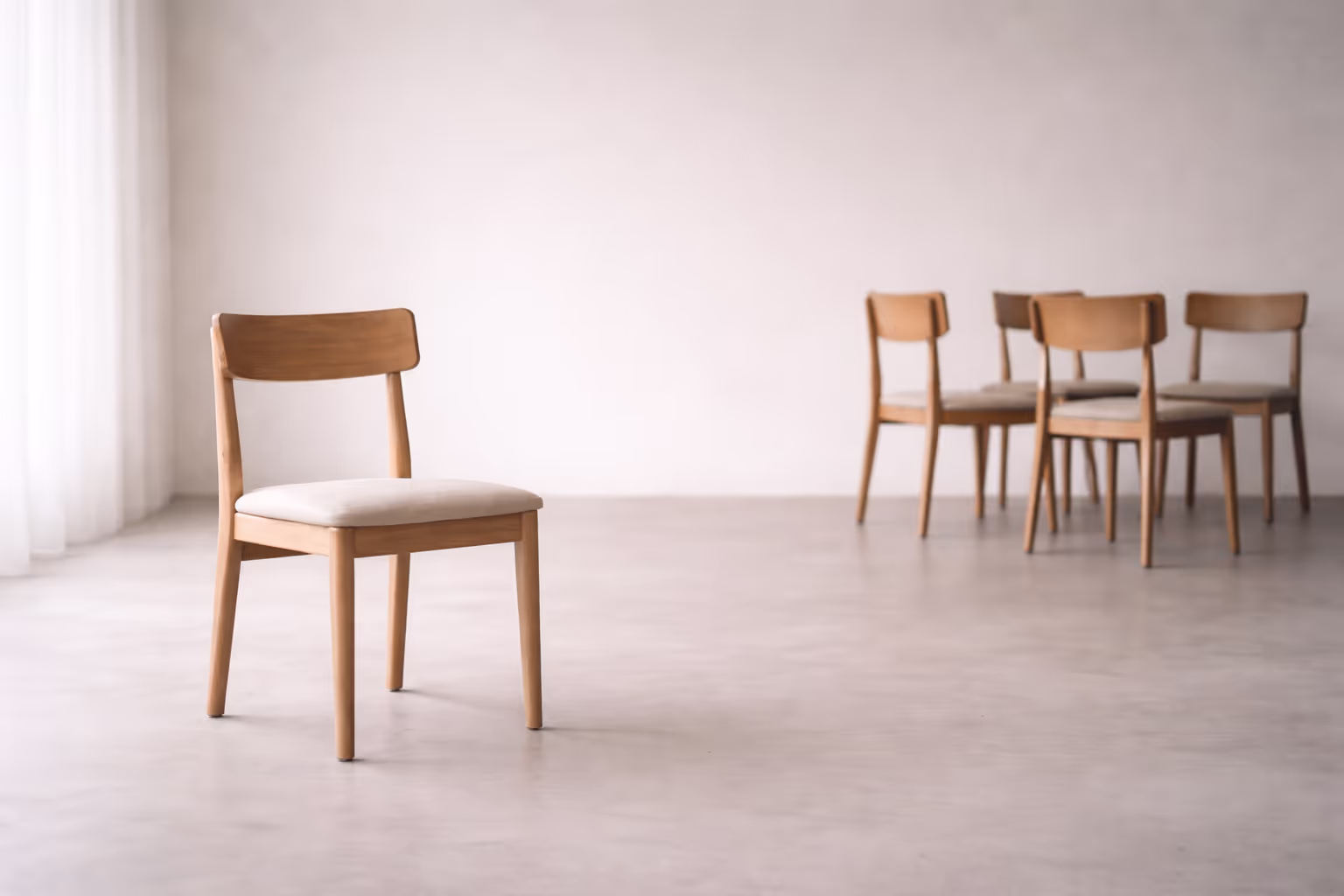 A single wooden chair slightly set apart from a small group of chairs, photographed in soft overcast light against a plain background.