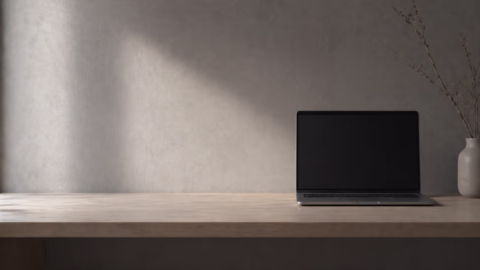 A bare desk surface with a closed or dark laptop, soft diffused light from one side, nothing else visible.