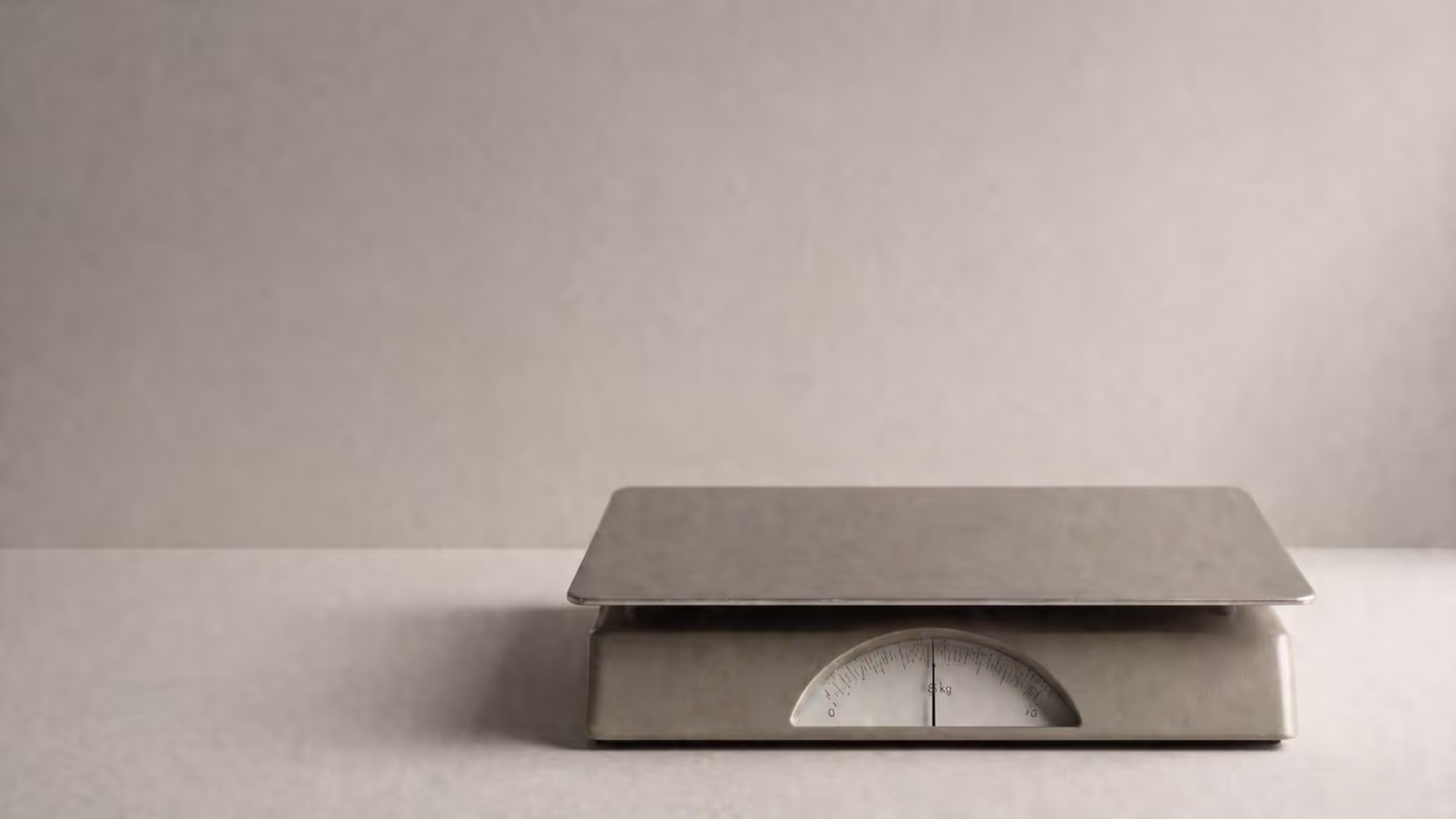 A single minimal scale or flat surface with subtle shadow, pale background, soft directional light, no objects on it, muted grey tones.