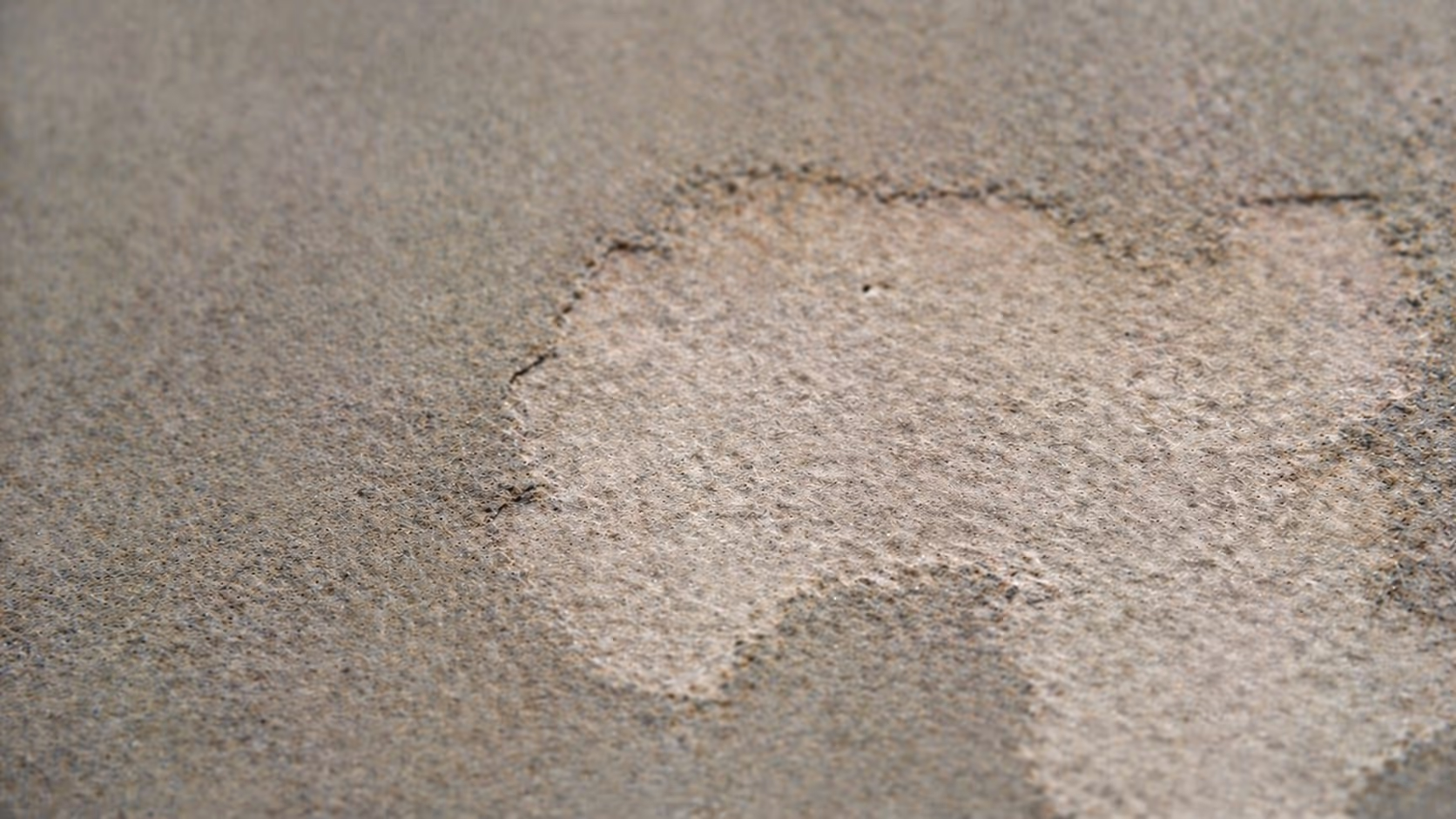 A close-up of a weathered stone surface, partially worn away to reveal a smoother, lighter layer underneath.