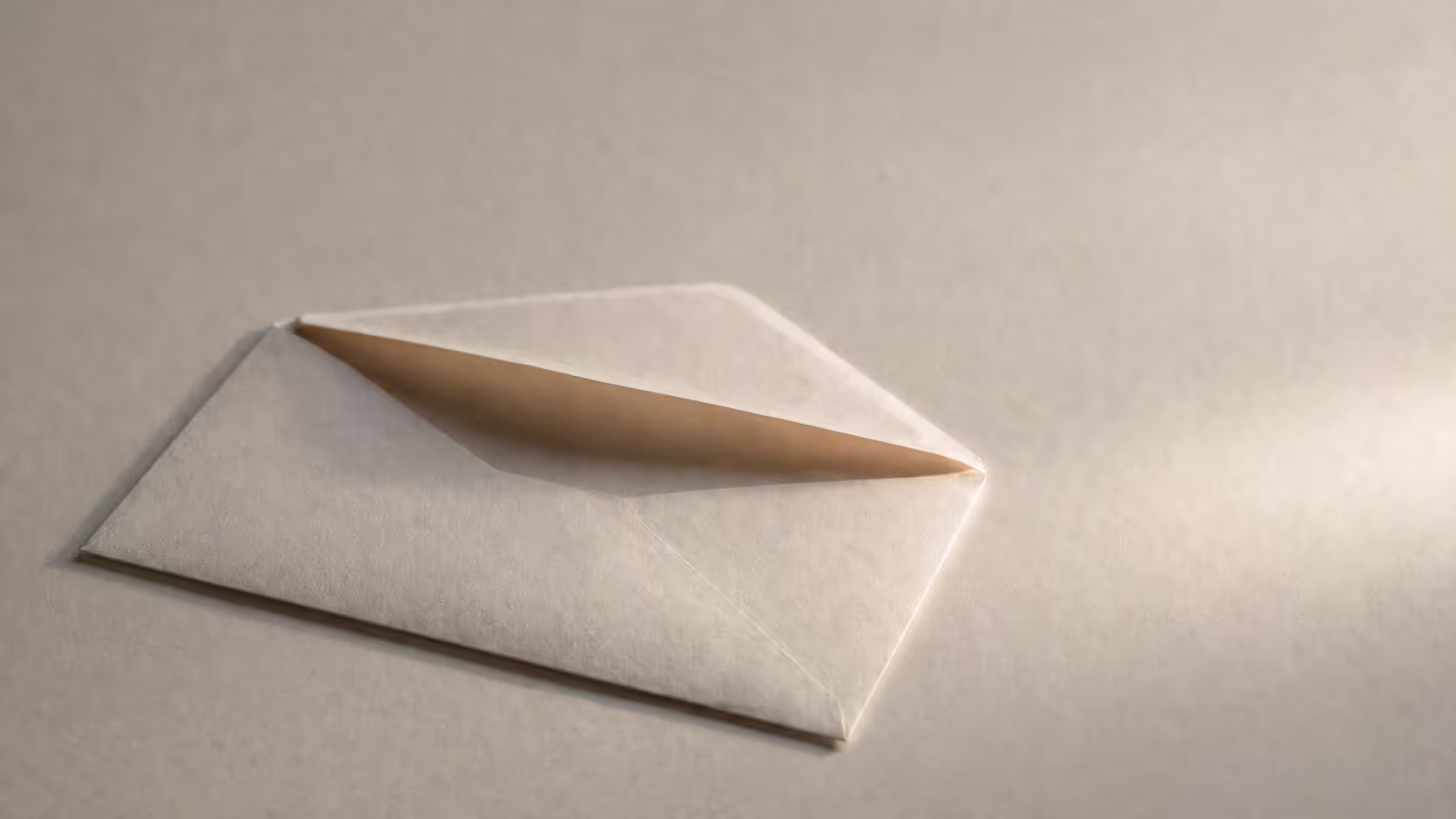 A single plain envelope, partially open, resting on a pale surface, soft directional light, no writing visible, muted warm tones.