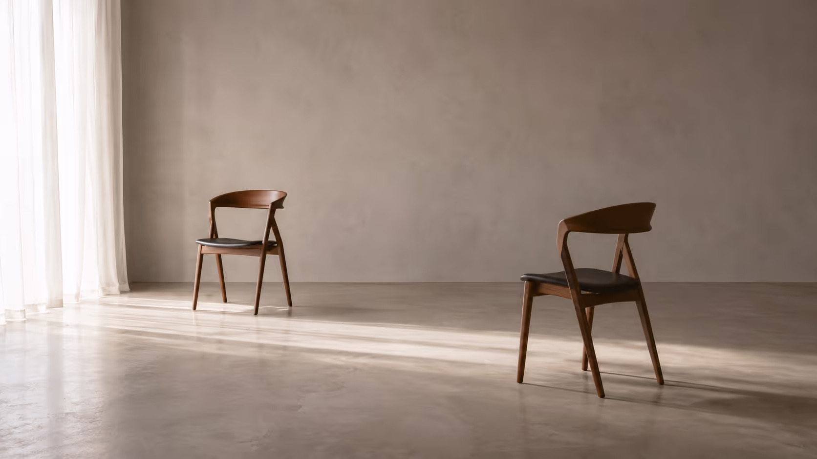 Two empty chairs in a softly lit room, placed at slight angles with substantial space between them.