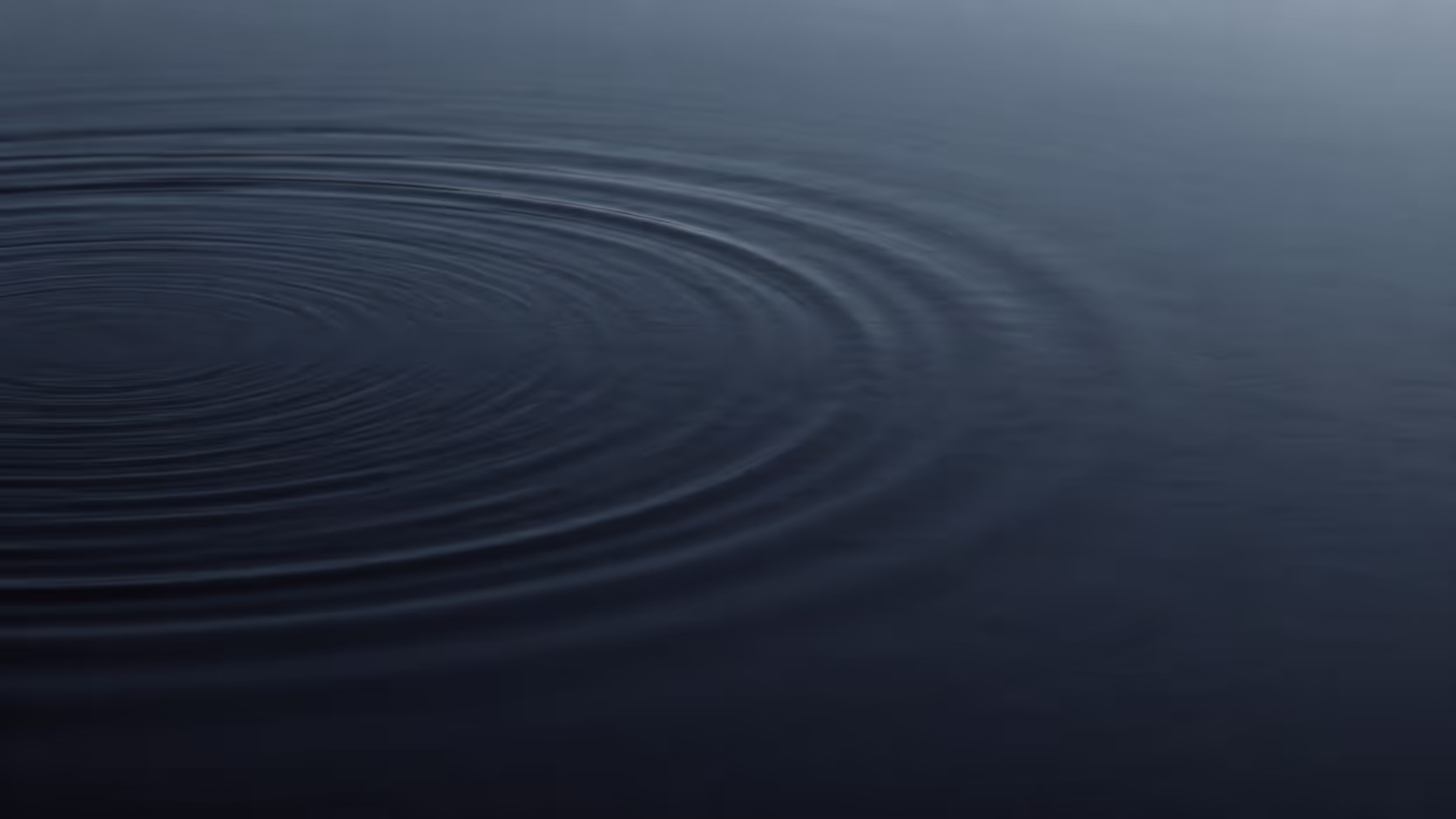 Concentric ripples spreading across the dark, still surface of water, originating from an unseen point near the edge of the frame.