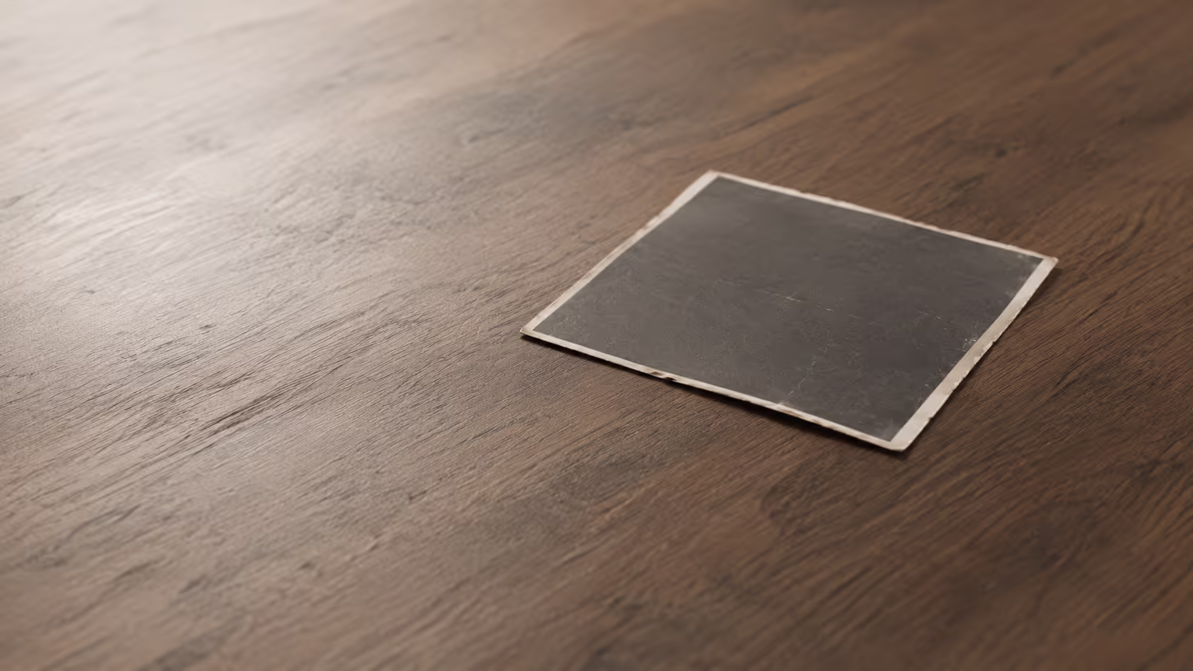 A single photographic print resting face-down on a plain wooden surface in soft diffused light.