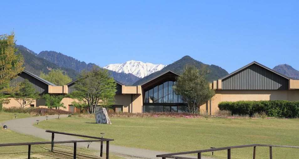 安曇野ちひろ美術館 広角で捉えた安曇野ちひろ美術館の風景。右側からのパースで、新緑の木々と特徴的な建築、雄大な山並みが美しく構成されている。