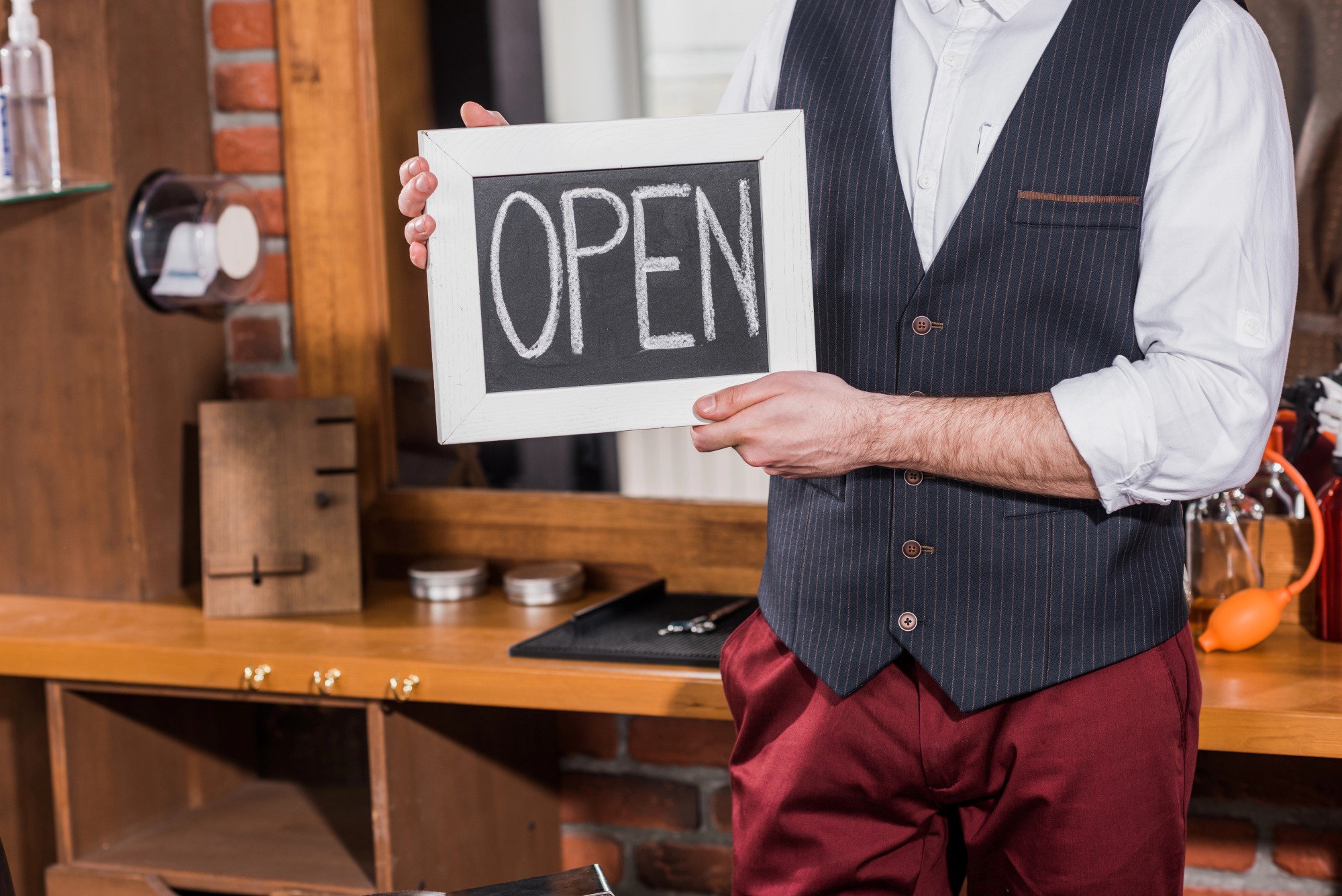 Cropped shot of barber holding open signboard in front of workplace