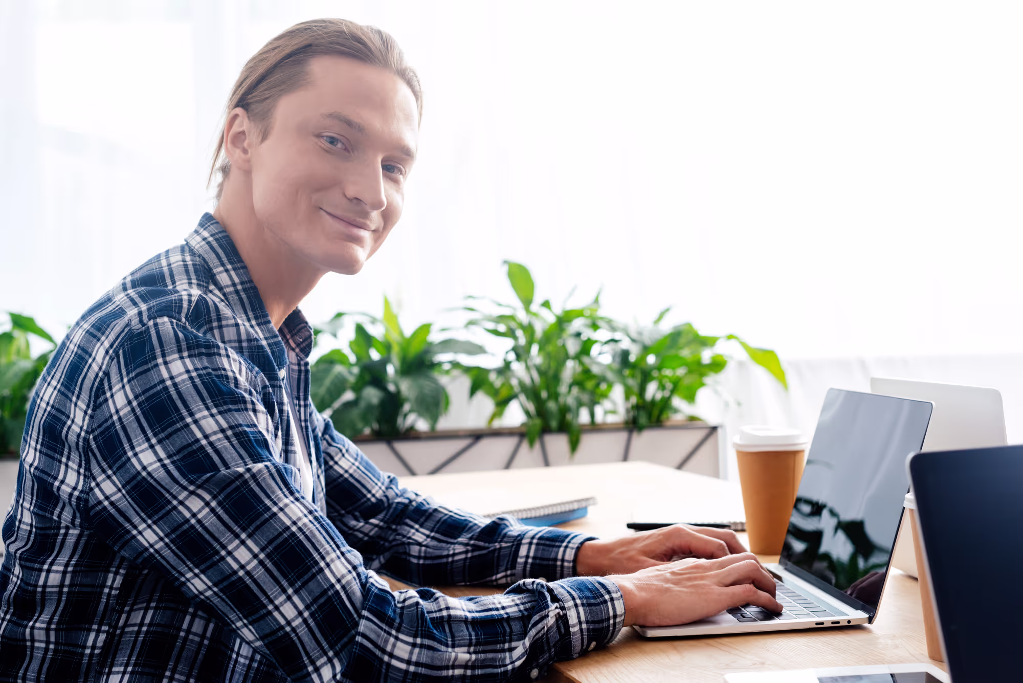 Young man using laptop and smiling at camera in office