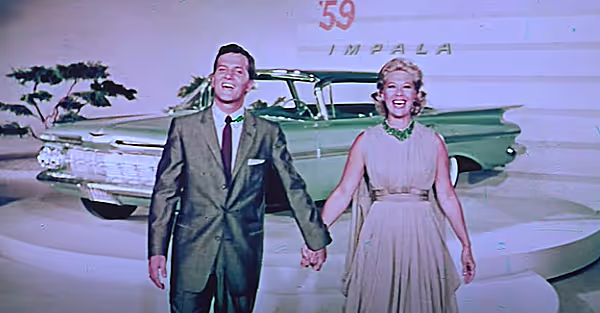 Celebrities in Vintage Car Ads. Still shot of a smiling man and Dinah Shore holding hands in front of a green 1959 Chevrolet Impala during a car commercial.