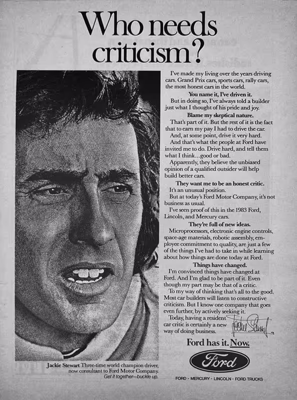 A black and white advertisement for Ford. On the left, a close-up portrait shows Jackie Stewart, a man with dark, wavy hair and an intense expression, looking slightly to the right with his mouth partially open as if speaking. To the right, a large headline reads 'Who needs criticism?'. Below it, body text discusses Ford's approach to feedback and innovation. At the bottom, the Ford oval logo is displayed, along with the slogan 'Ford has it. Now.' and a caption identifying Jackie Stewart as a 'Three-time world champion driver, now consultant to Ford Motor Company.'