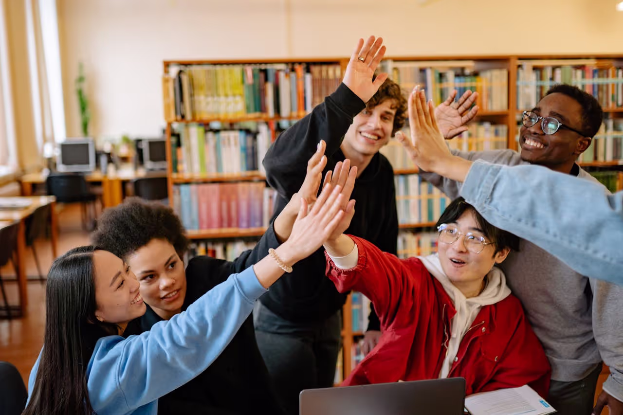 A group of college freshmen giving high fives and having fun while planning an exciting campus event, demonstrating teamwork and key freshman year college tips.