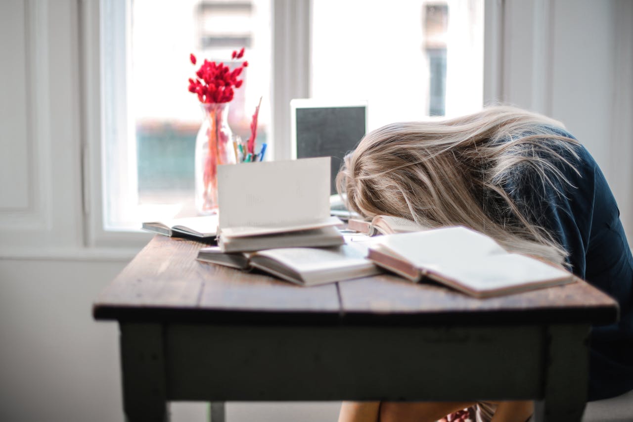 College student resting his head on a desk while studying, appearing stressed and overwhelmed, illustrating the importance of supporting college student mental health from distance.