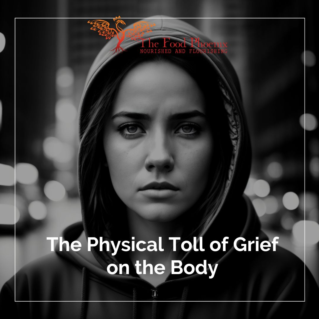 Black-and-white image of a serious young woman in a hoodie on a city street with blurred lights, overlaid with the text 'The Physical Toll of Grief on the Body' and a phoenix logo reading 'The Food Phoenix – Nourished and Flourishing' at the top.