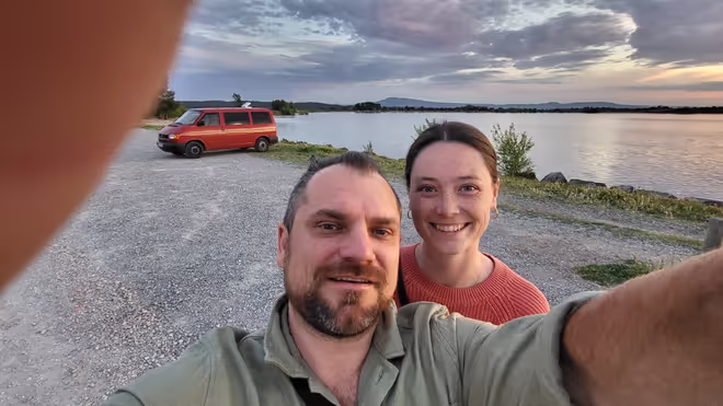 Konrad and Caro by a lake in France, with their VW T4 behind them