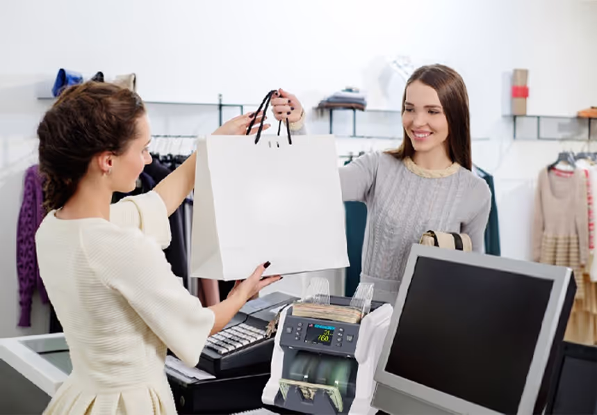 A smiling woman cashier at a retail store handing a bag to a customer, with a Ribao BC-40 money counter on the counter.