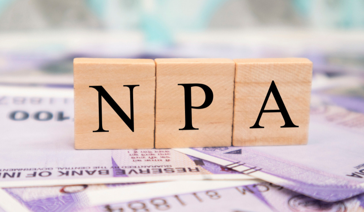 Becomes Non-Performing Assets Three wooden blocks spelling 'NPA' (Non-Performing Asset) arranged on a scattered pile of Indian rupee banknotes.
